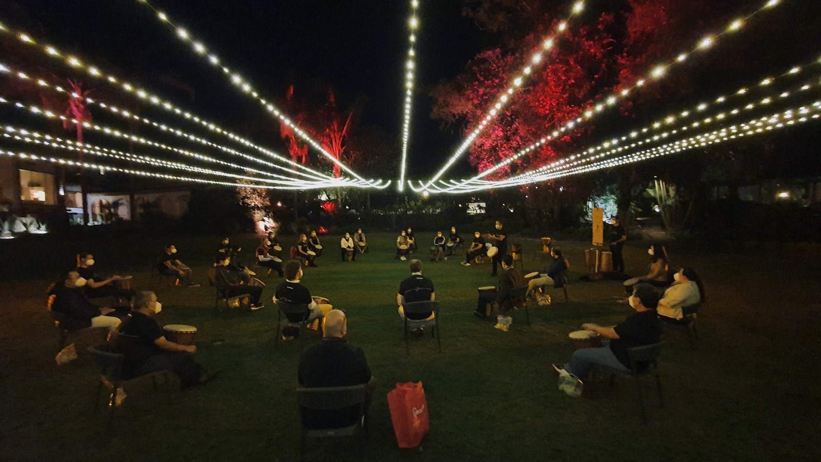 Círculo de percusionistas al aire libre bajo guirnaldas de luces